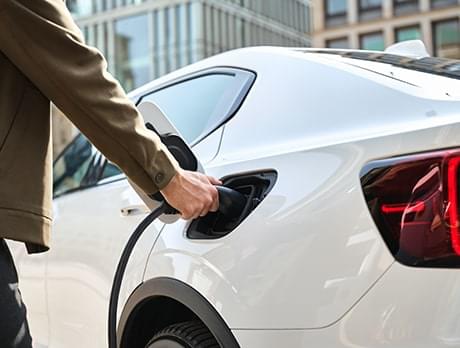 Jemand steckt den Ladestecker in ein Elektroauto um den Ladevorgang zu starten